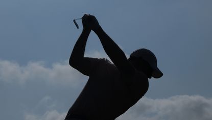 Silhouette of Rory McIlroy at the top of his backswing with an iron, against a blue sky background