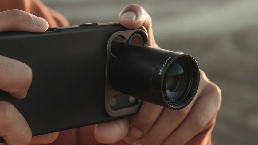 A person is holding a black smartphone with an external camera lens attachment, labeled &quot;SANDMARC,&quot; connected to the phone&#039;s main camera module.
