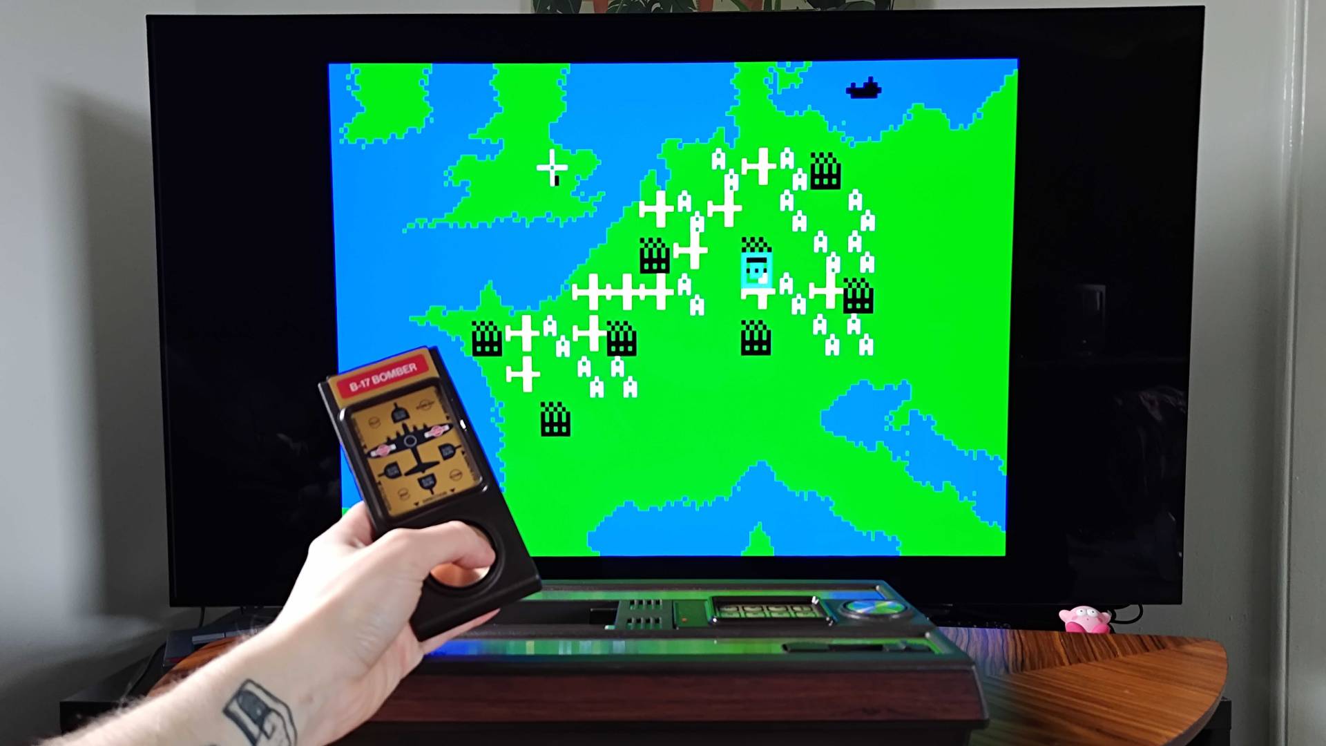 Hand holding Intellivision Sprint controller with B-17 Bomber gameplay in backdrop.