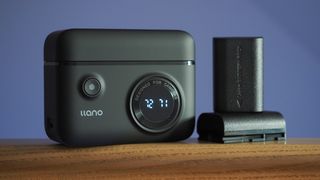 The Llano Dual Camera Battery and Charger set on a wooden surface against a purple background