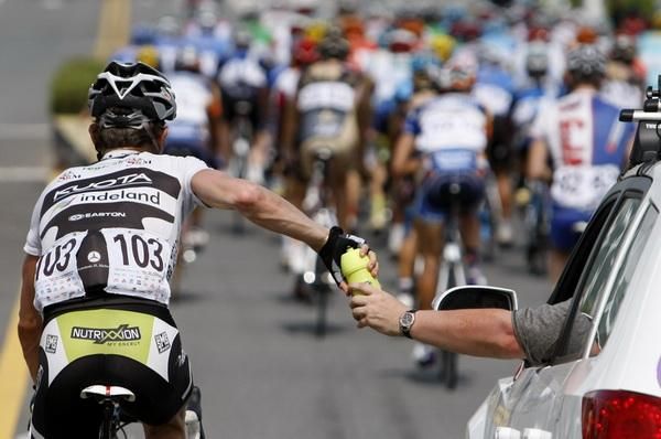 A Team Kuota - Indeland rider collects some water bottles from the team car.