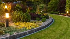 Professionally Landscaped Backyard Garden with Evenly Mowed Lawn and Trimmed Shrubs Illuminated with Outdoor Bollard Lamps - for article on 'how much does landscaping cost for small, medium and big yards