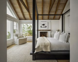 A bedroom with wooden beamed ceilings, white wall panels with millwork, and a black four poster bed
