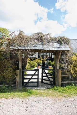lychgate with rustic gate and shrubs and climbers above and barn building behind