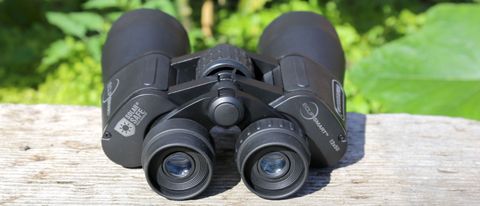 Celestron EclipSmart 12x50 porro solar binoculars placed on a wooden surface with green foliage behind