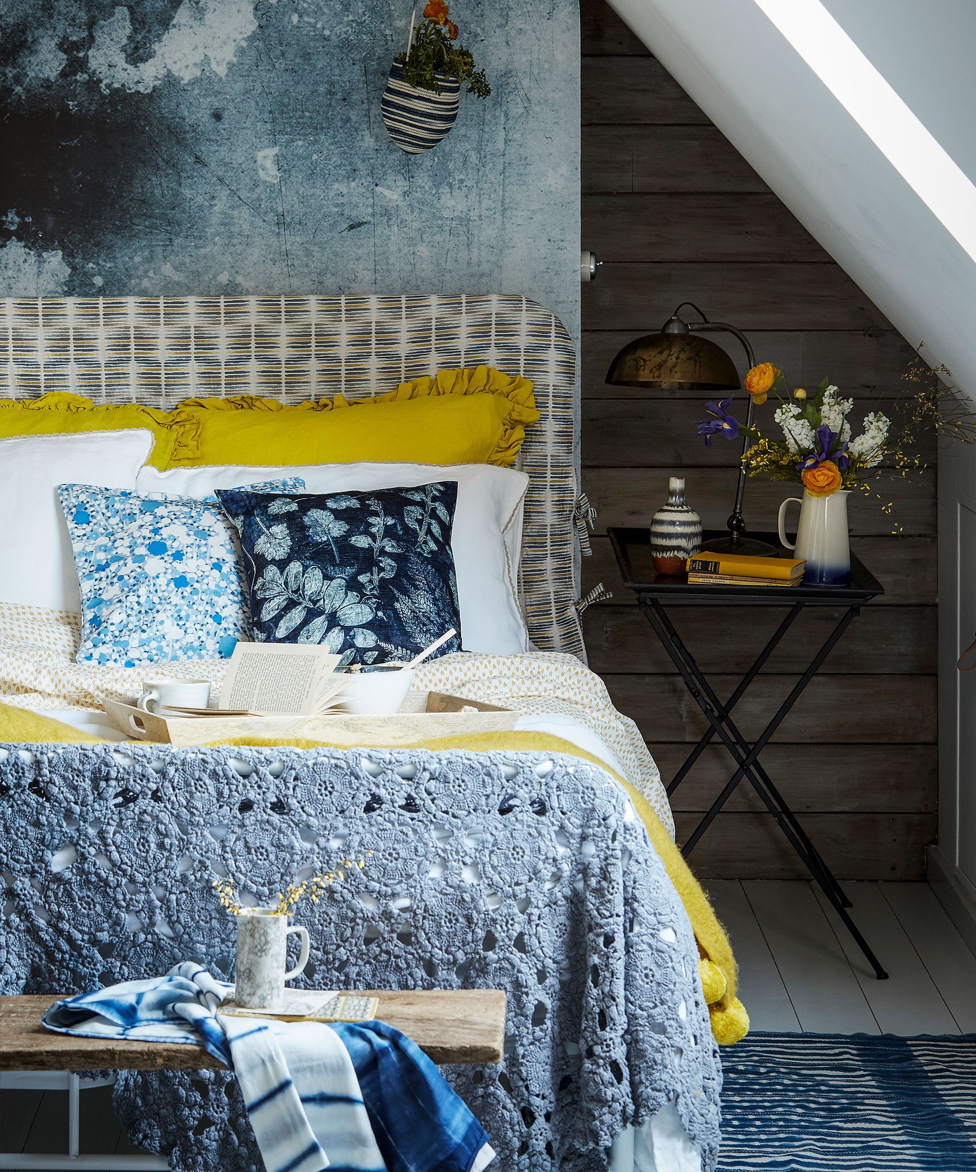 A bed with a gray and white patterned headboard and yellow bedding next to a black bedside table