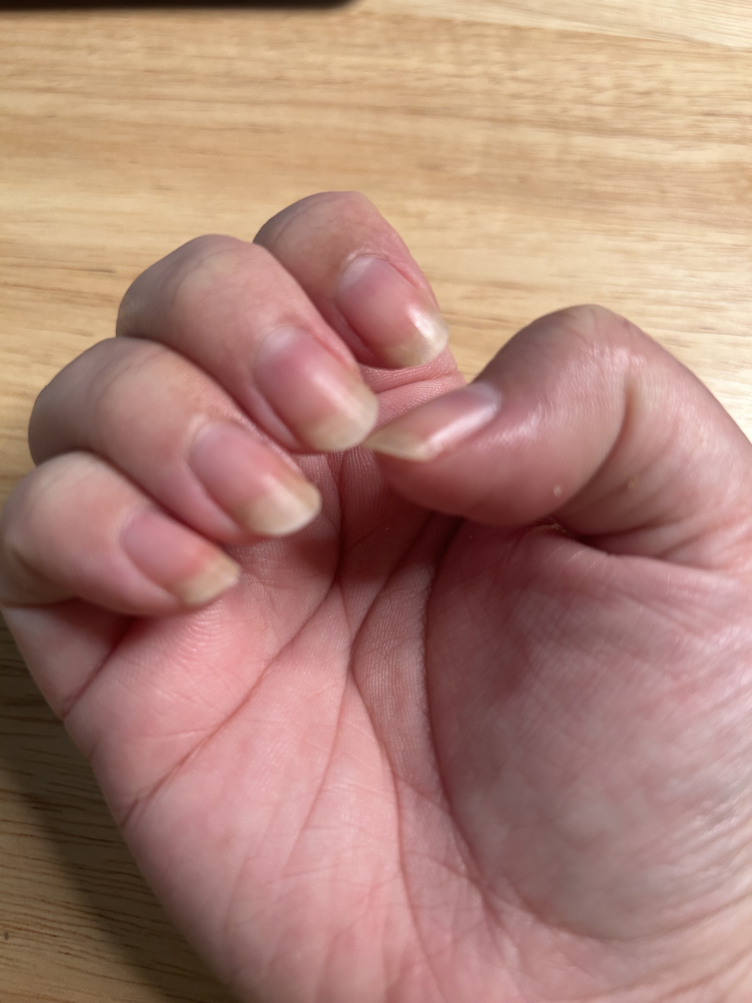 A woman's hand and nails before applying cuticle oil with a wood background.