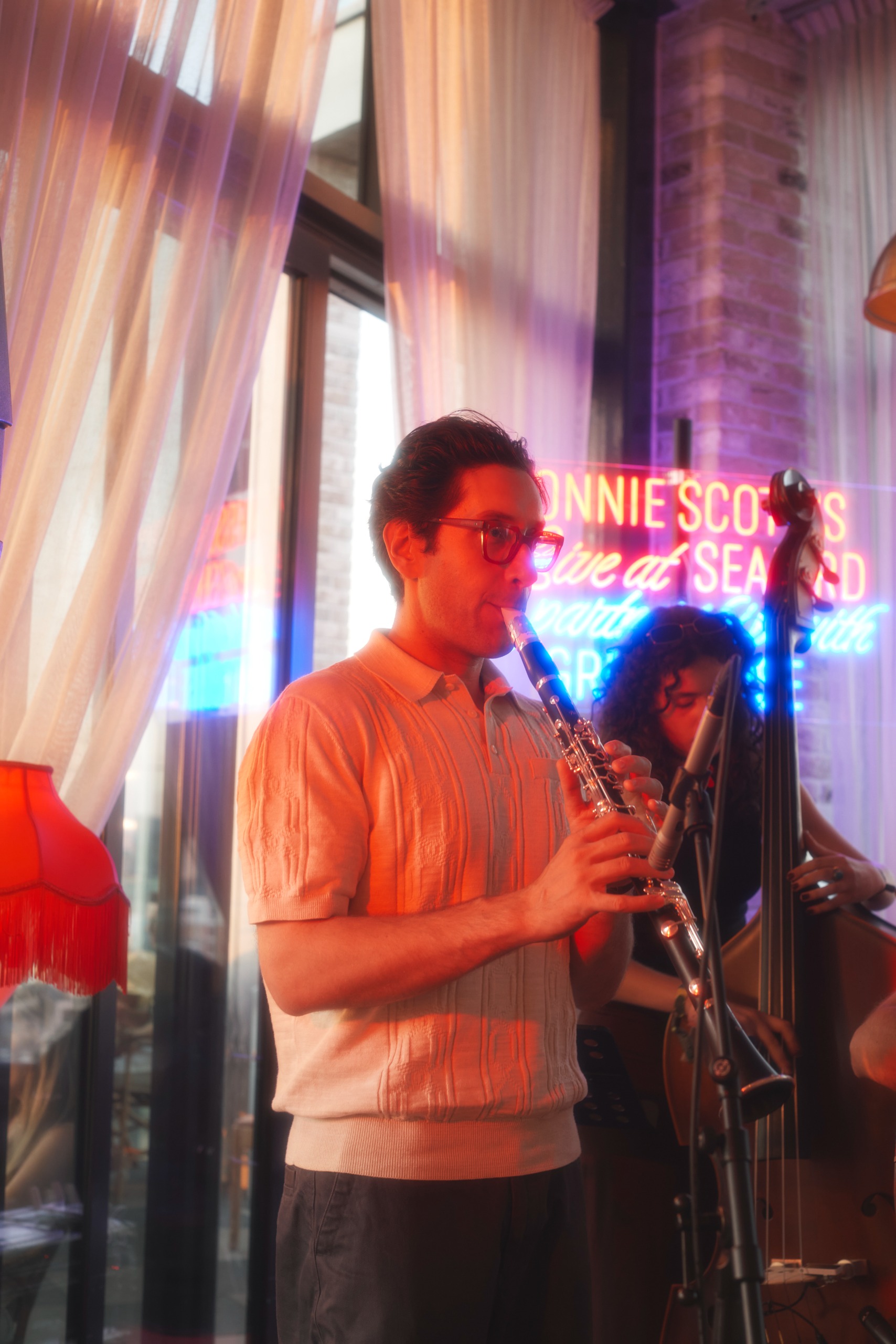 Photos of a live jazz performance happening inside a glamorous rooftop bar decked out with red-tinted table lamps, neon lights, and palms.