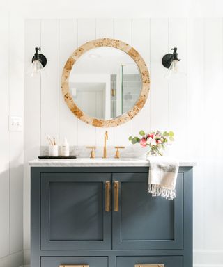 Bathroom with white shiplap paneling and dark grey vanity with circular bathroom mirror and wall lighting