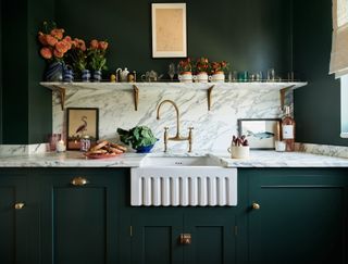 dark green kitchen with marble backsplash and counter with apron sink