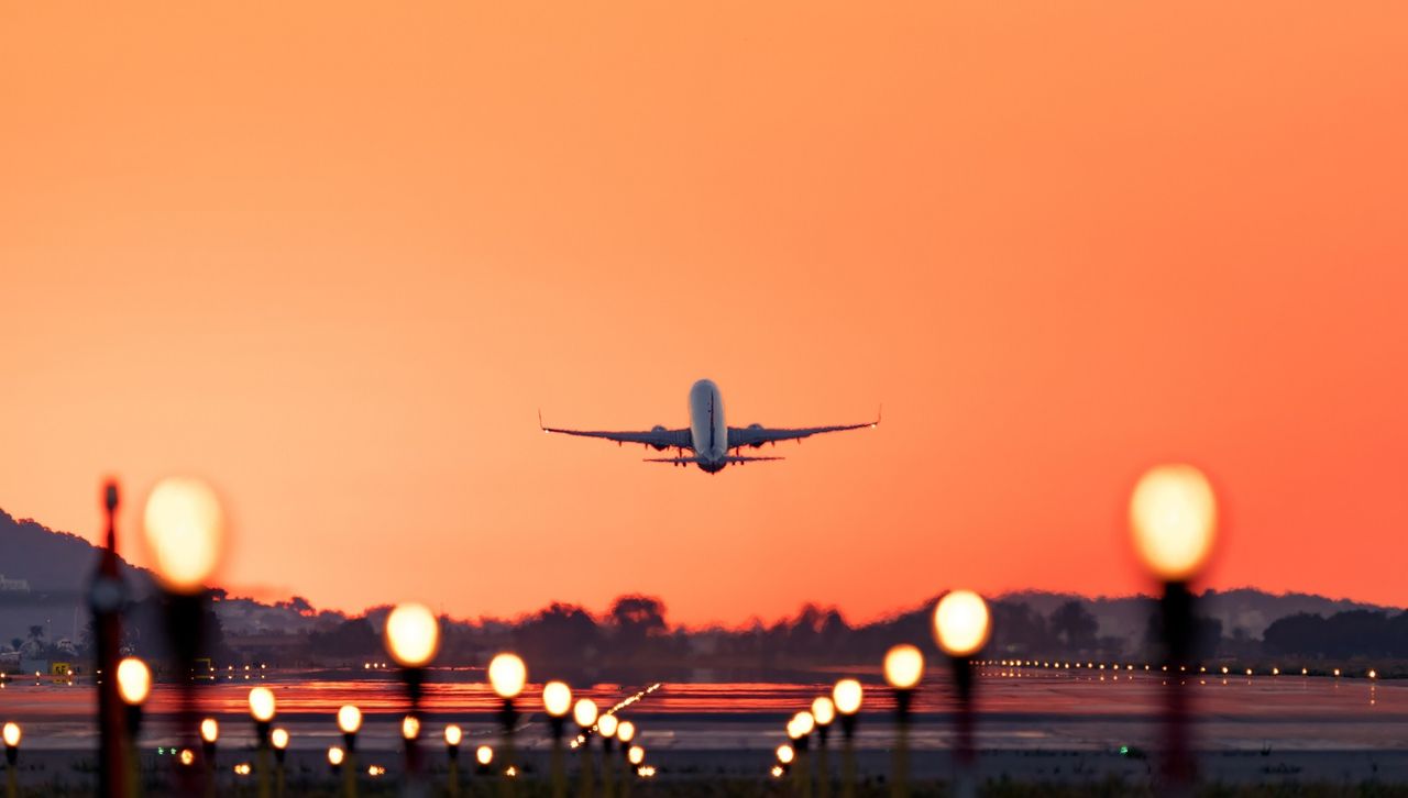 A plane taking off from a runway as the sun rises. 