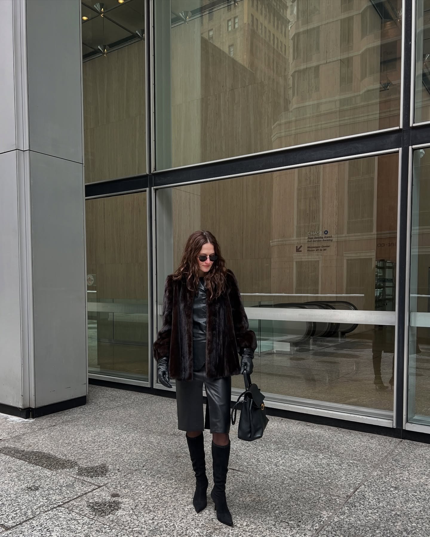 Eliza Huber wearing a skirt outfit idea for 2026, including a fur jacket, black leather blazer, black leather pencil skirt, and knee-high boots.