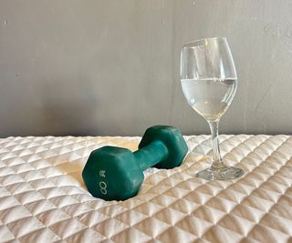 A wine glass full of water next to a weight on a mattress.