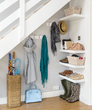 Under-the-stairs storage, with wall-mounted shelves topped with clothing and shoes and a basket stand with umbrellas