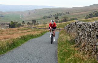 Cyclist Simon Warren climbing on a UK road with a dry stone wall to his right