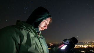 A man looking down at a Fujifilm X-T50 with stars and streetlights in the background.
