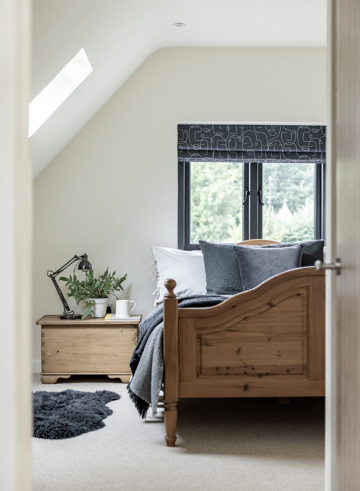 A bedroom with a sloped ceiling and rooflights, a wooden double bed and a wooden bedside table with a lamp on it