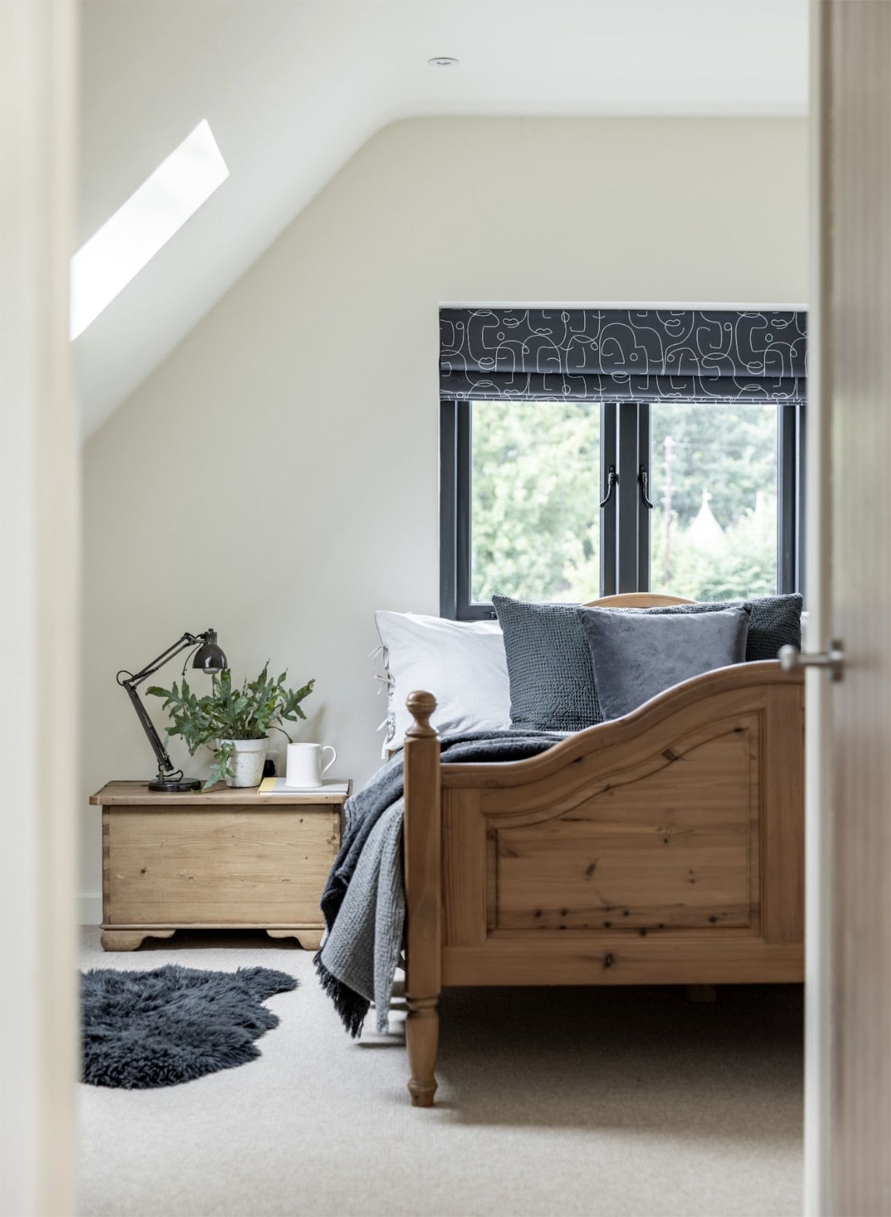 A bedroom with a sloped ceiling and rooflights, a wooden double bed and a wooden bedside table with a lamp on it