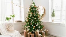 An image of a Christmas tree with neutral colored ornaments in a bright living room surrounded by presents