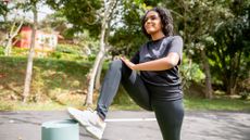 Woman wearing black sportswear in a park with her foot resting on a bollard