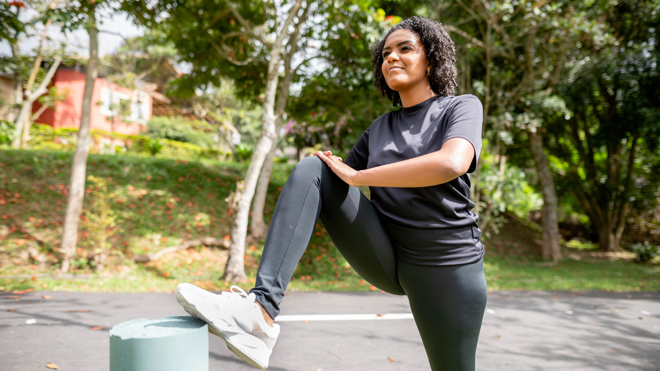 Woman wearing black sportswear in a park with her foot resting on a bollard