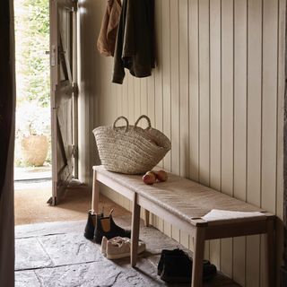 hallway with bench, shoes underneath, front door open, coats hanging up, basket, cream tongue & groove walls, stone floor