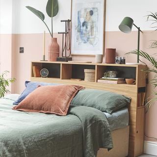 Pink bedroom with green duvet set. There is a shelf built into the headboard with books, a clock and house plant.