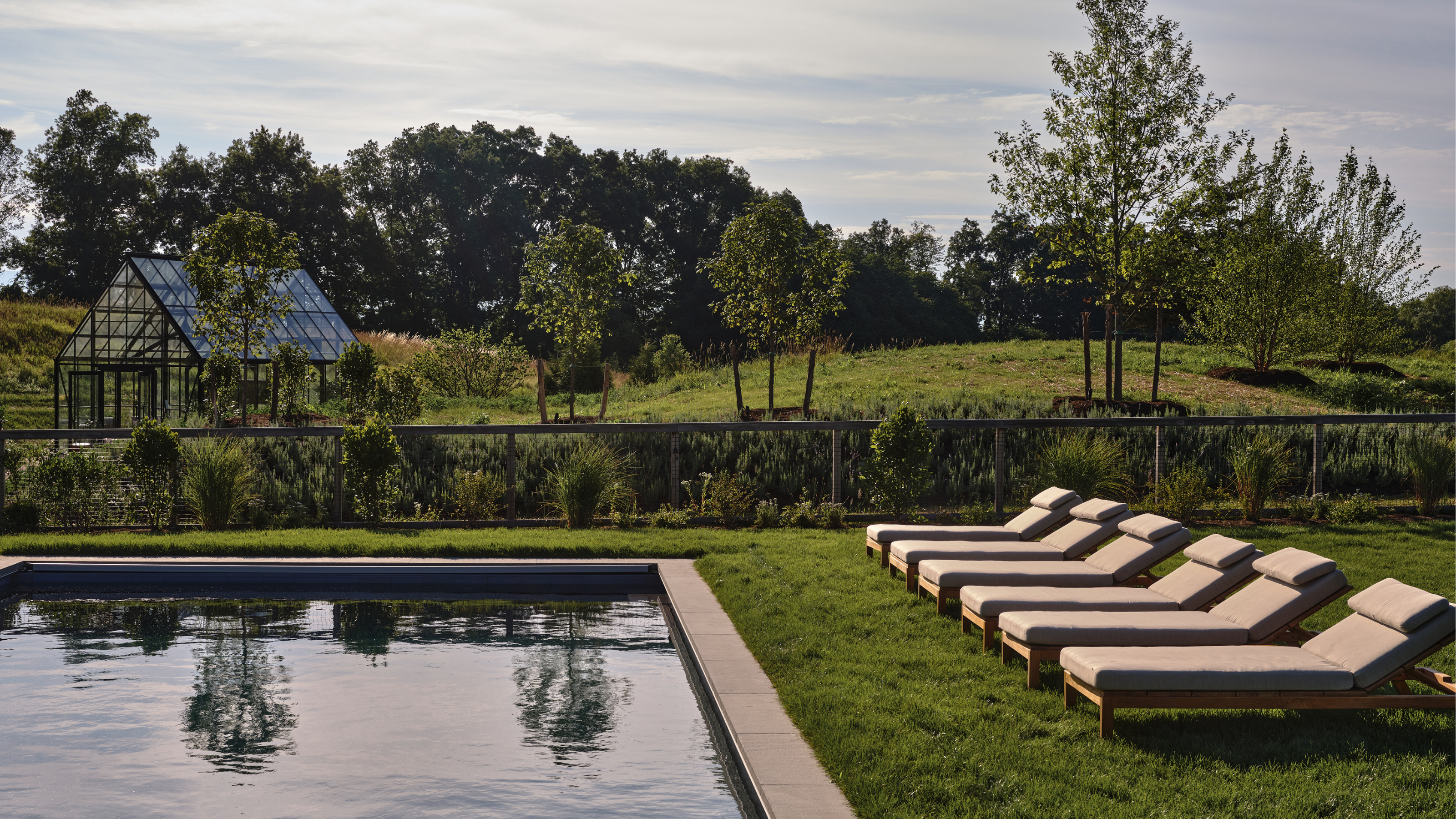 in-ground pool surrounded by grass and lined with six chaise lounge chairs