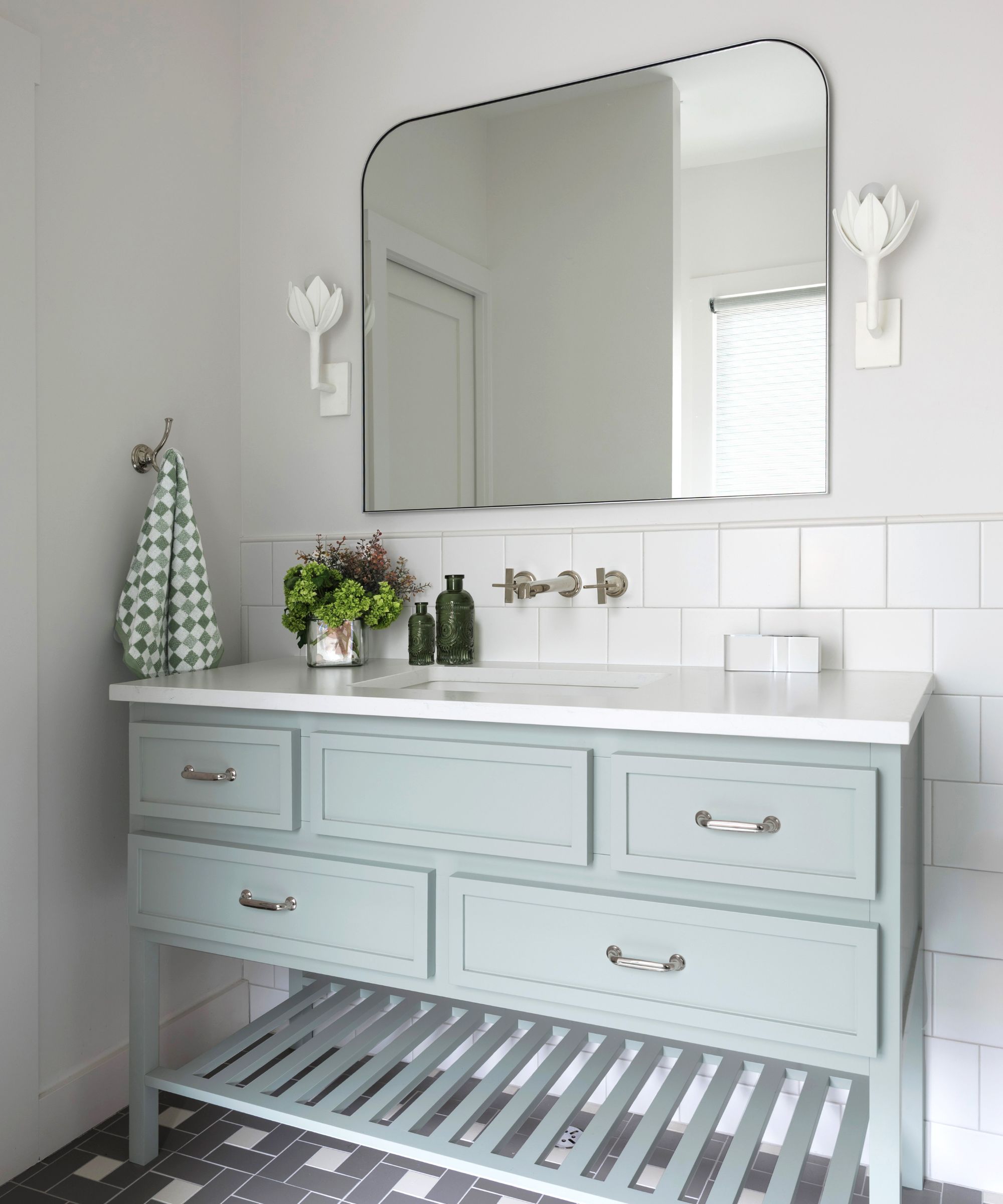 A white bathroom with a light blue bathroom vanity and white flower sconces on the walls