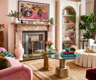 maximalist living room with large tall marble fireplace and fire, pink walls, artwork on chimney breast above fireplace