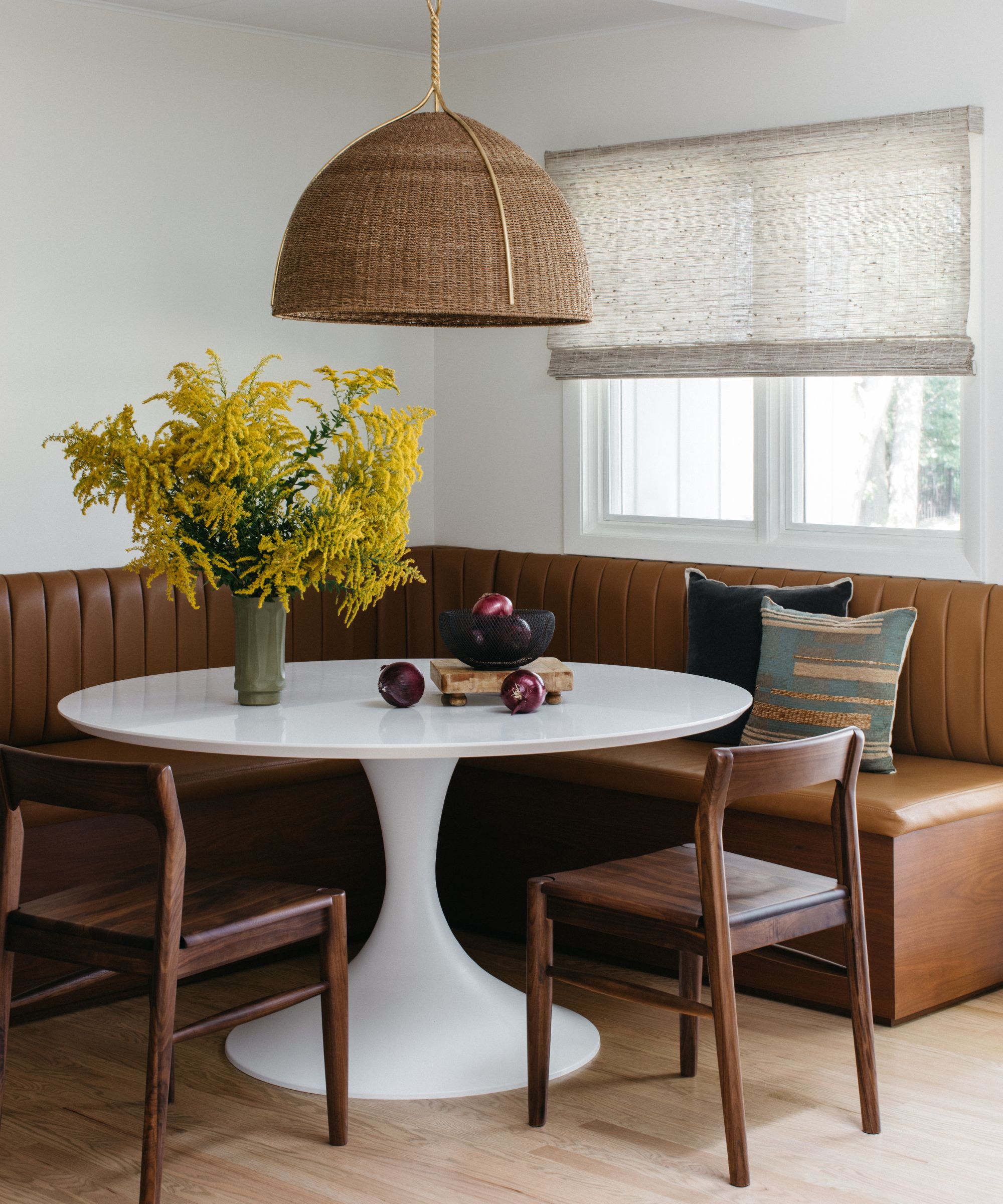 A kitchen corner with a brown leather banquette, a round white table, and two wooden chairs
