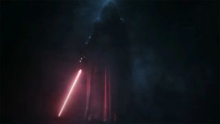 Still from the trailer for the video game Star Wars: Knights of the Old Republic remake. A robed, mysterious figure is standing in darkness. The only source of light is the red lightsaber they are holding, which is pointed towards the ground.