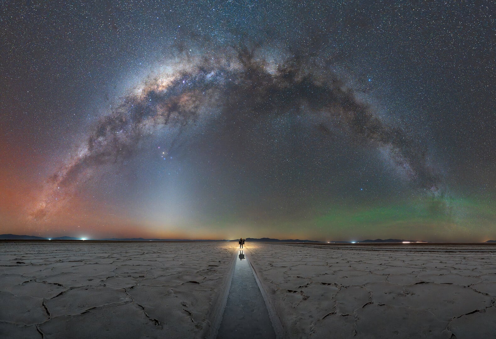 A photo of the Milky Way visible as an arc in the sky above desert salt flats