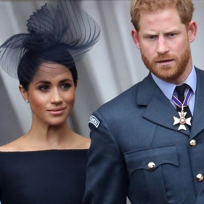 Queen Elizabeth wears a blue and turquoise coat and matching hat as she stands on the Buckingham Palace balcony with Meghan Markle, the Duchess of Sussex, who is wearing a black outfit, and Prince Harry, who is wearing military uniform