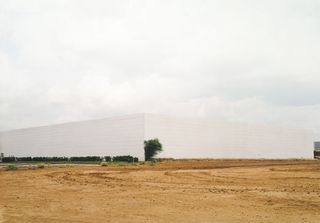 An eye level view of a white building surrounded by waste land.