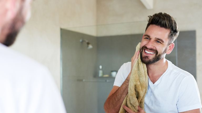 A man looking in the mirror, drying his beard after applying the best beard oil