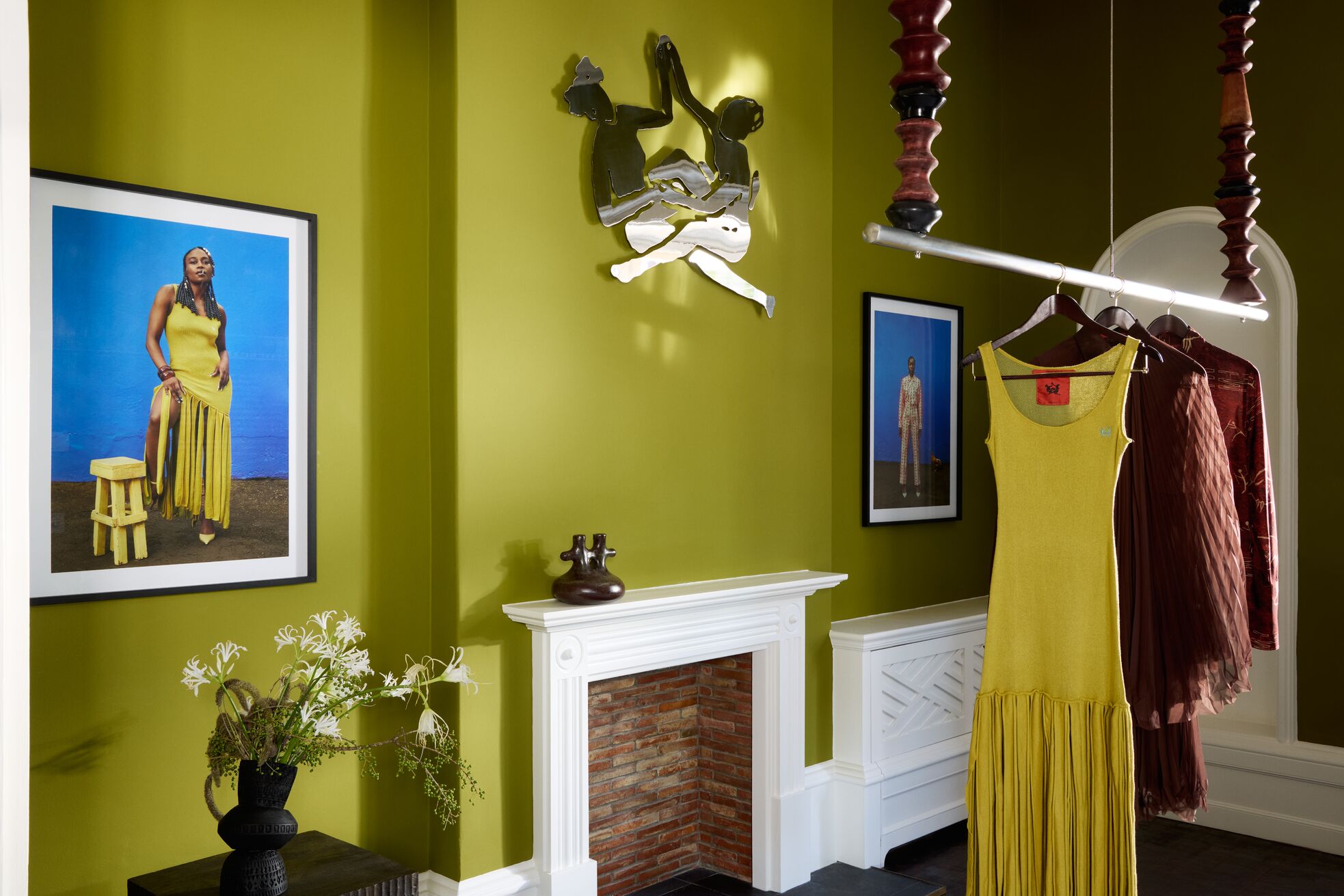 A series of shots capturing a young man dressed in patterned, or color-blocky, clothing, either standing in the sun-lit outdoor areas of a lush hotel, or inside a colorfully decorated suite filled with collectibles, artworks, and textural touches, or the interiors of that very space.