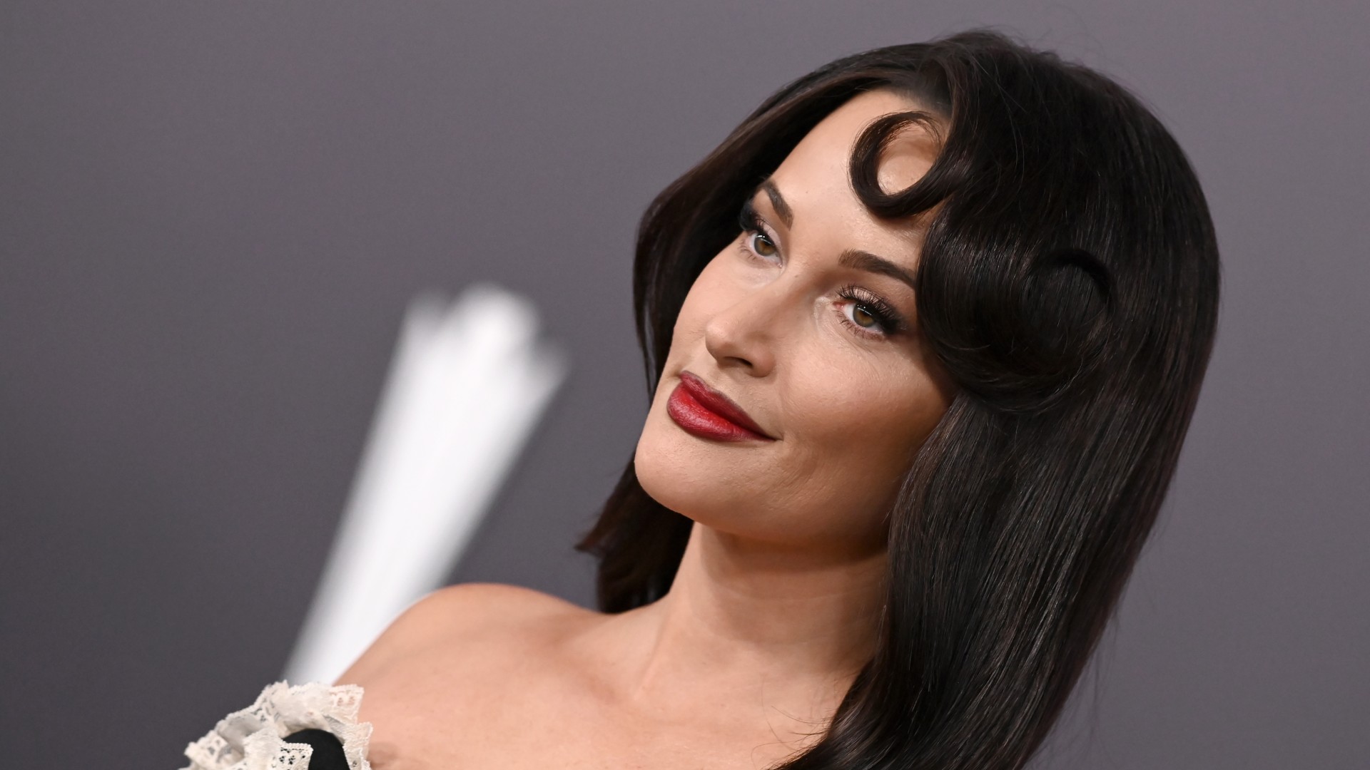 a white woman with dark hair poses in front of a gray backdrop at a red carpet event
