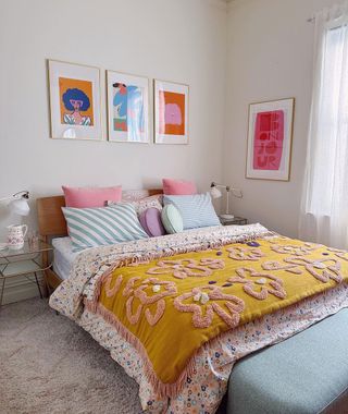 Eclectic bedding with mustard throw contrasting light blue hues on pillows and row of three artwork pieces framing headboard