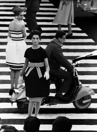 black and white photo of a lady wearing a dark dress with white and black striped bow, walking down the Spanish steps whilst another lady wearing a white dress lined with stripes looks back at her