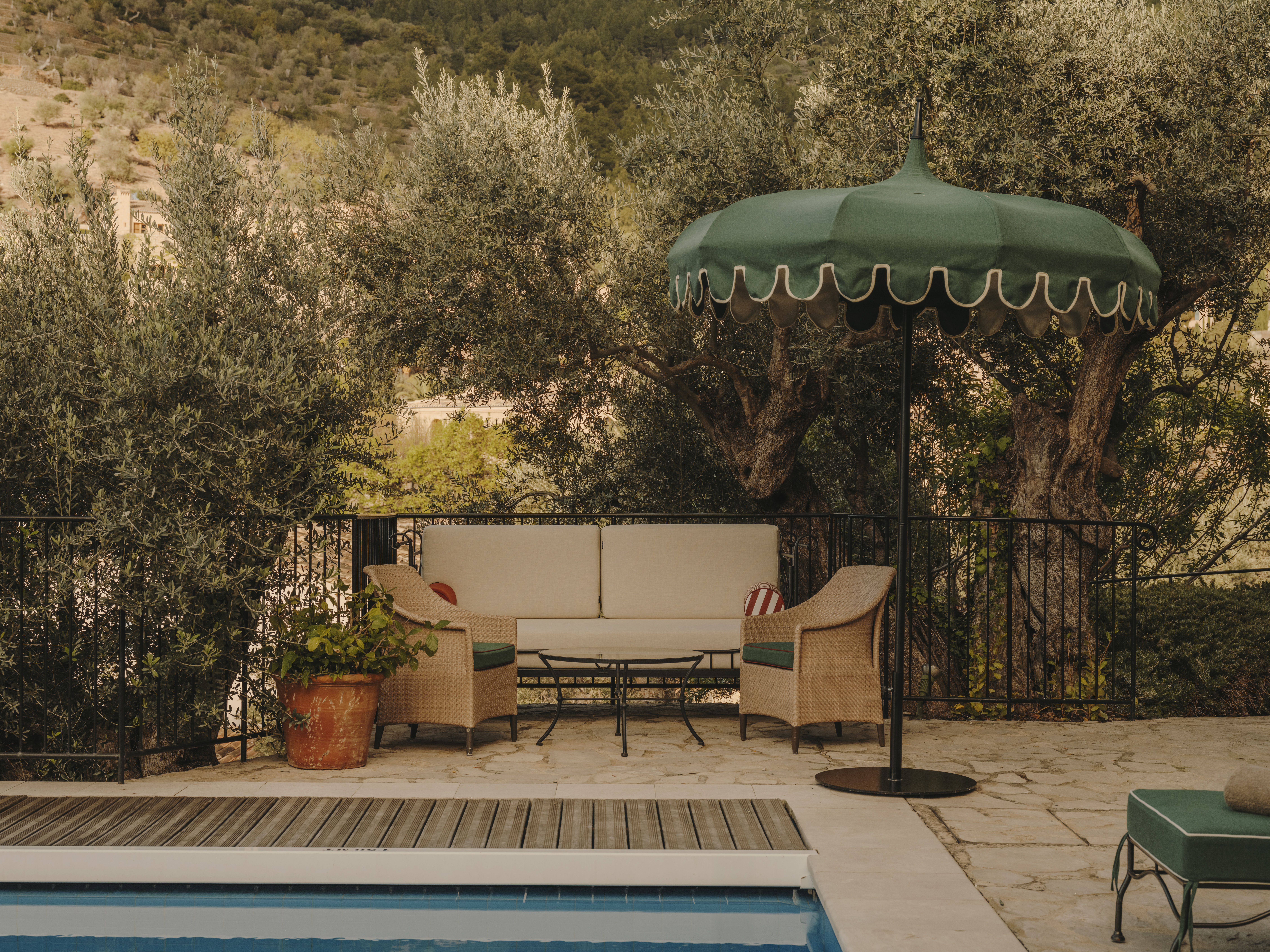 A private pool immersed in greenery and decorated with green, vintage-looking parasols bakes in the summer sunshine.