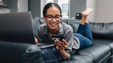 woman on the couch online shopping with credit card in hand