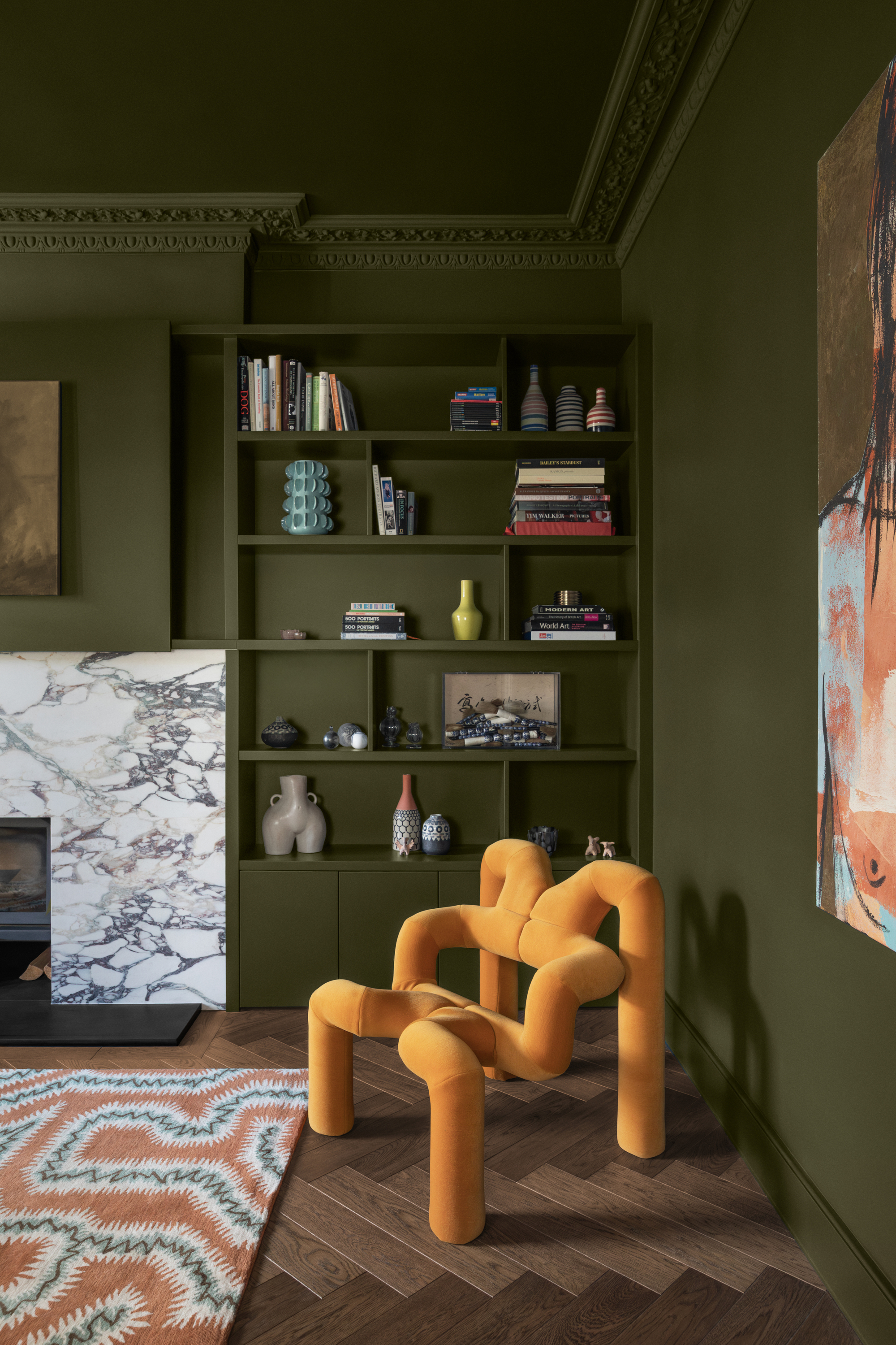 Image of a living room color drenched in an olive green. There is an abstract, yellow accent chair in the corner with a white marble fireplace.