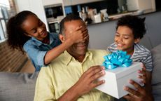 Photo of father opening gift box as two young children watch