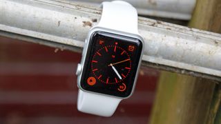 The Apple Watch with a white strap showing a red watch face.