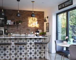 A small kitchen with yellow 'Let's stay Home' neon sign