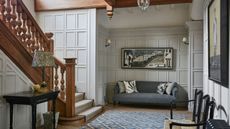 Arts & Crafts hallway with wood staircase, wall panelling, rug on floor, paint work and grey sofa