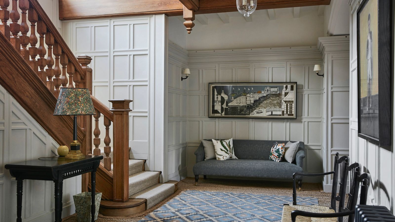 Arts &amp; Crafts hallway with wood staircase, wall panelling, rug on floor, paint work and grey sofa