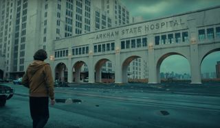 Joker Arthur walking up to decrepit Arkham State Hospital