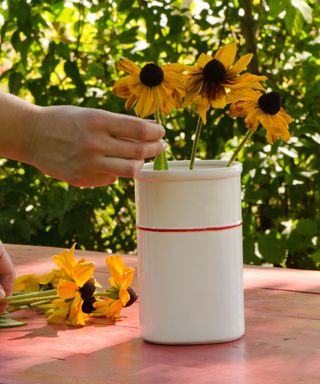Woman's hand placing black-eyed Susans in a pottery vase on a table